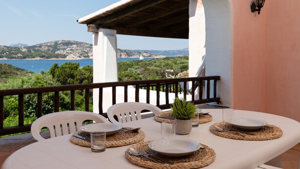Une table dressée en plein air, avec vue sur la mer, des chaises blanches et une plante en pot.