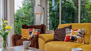 Una sala de estar moderna con un sofá, un sillón y una mesa con revistas, un plato de galletas y un jarrón de flores.