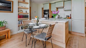 Una cocina moderna con una isla central, estantes empotrados y un comedor con sillas de mimbre.