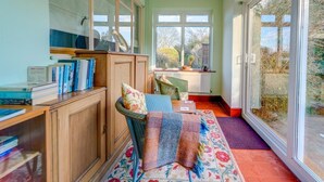 Une pièce dotée d’une grande fenêtre, d’une bibliothèque, d’un fauteuil en osier et d’un tapis à motifs.