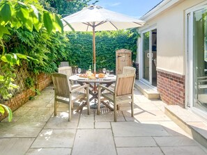 An outdoor patio with a round table and chairs, a wooden cabinet, and a large umbrella. - 3 Bed in Totland Bay (oc-ic110) (Totland)