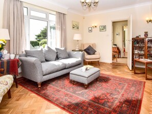 A living room with a grey sofa, a red patterned rug, a wooden coffee table, and a chair. - 3 Bed in Totland Bay (oc-ic110) (Totland)