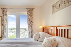 A hotel room with a bed, floral curtains, a view of buildings, and a wooden headboard. - 3 Bed in Shanklin (oc-ic113) (Shanklin)