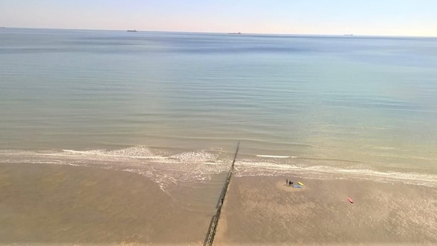 Una spiaggia con acque calme, una riva sabbiosa e alcune persone e oggetti sulla sabbia.