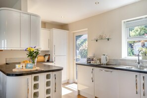 A modern kitchen with white cabinetry, a curved countertop, and a window providing natural light. - 3 Bed in Shanklin (oc-ic113) (Shanklin)
