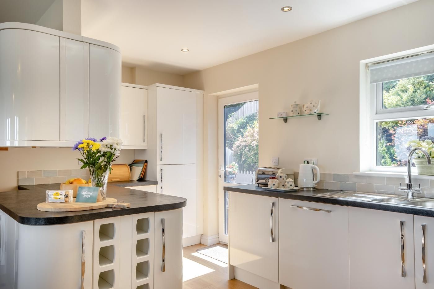 A modern kitchen with white cabinetry, a curved countertop, and a window providing natural light.