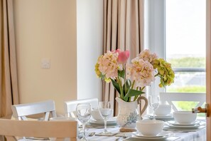 A dining table set with white plates, bowls, and wine glasses, with a vase of flowers in the center. - 3 Bed in Shanklin (oc-ic113) (Shanklin)