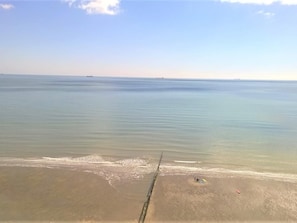 Una playa con aguas tranquilas, una orilla arenosa y algunas personas y objetos sobre la arena.