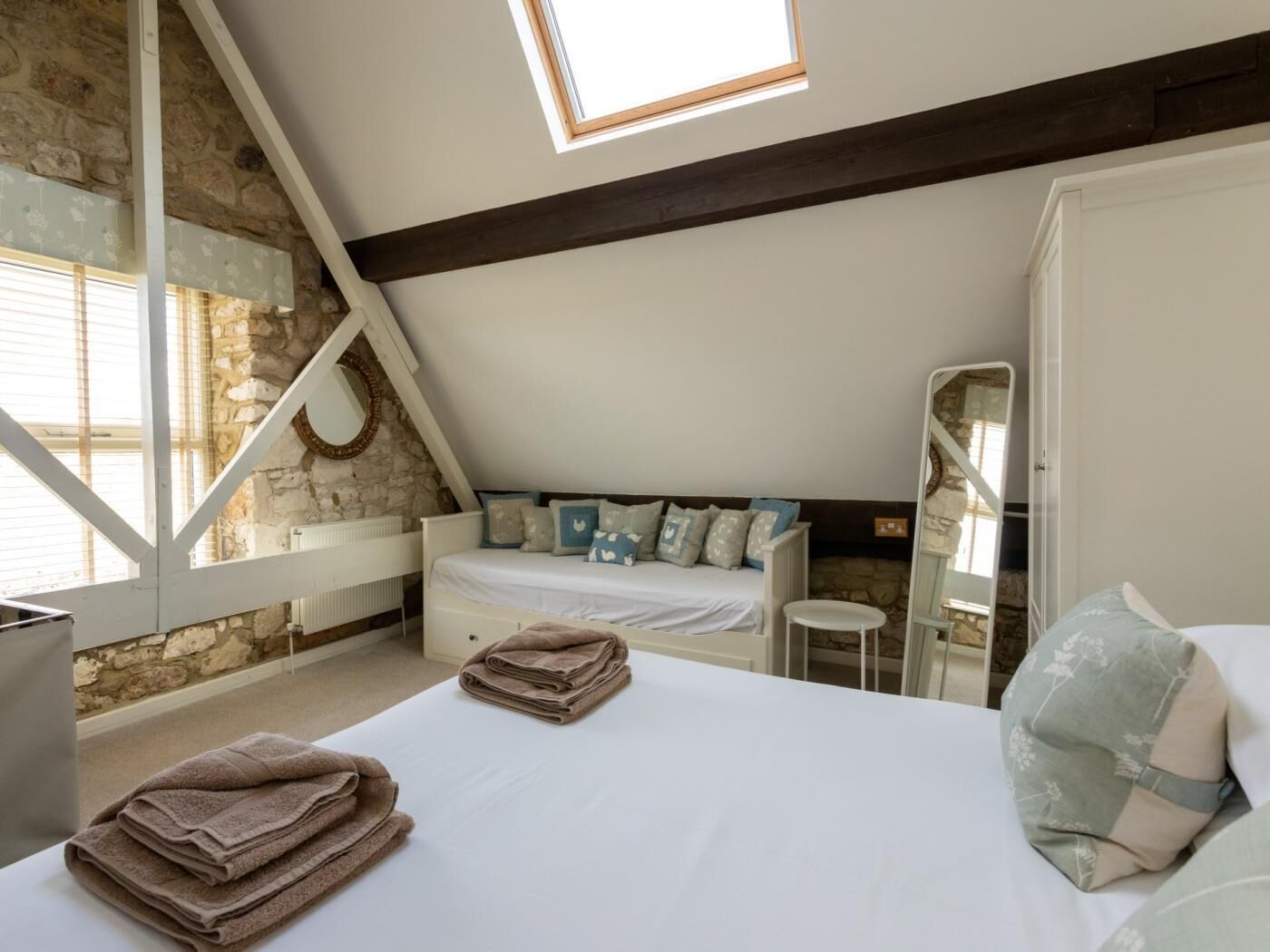 A bedroom with a sloped ceiling, stone wall, and a bed with pillows.