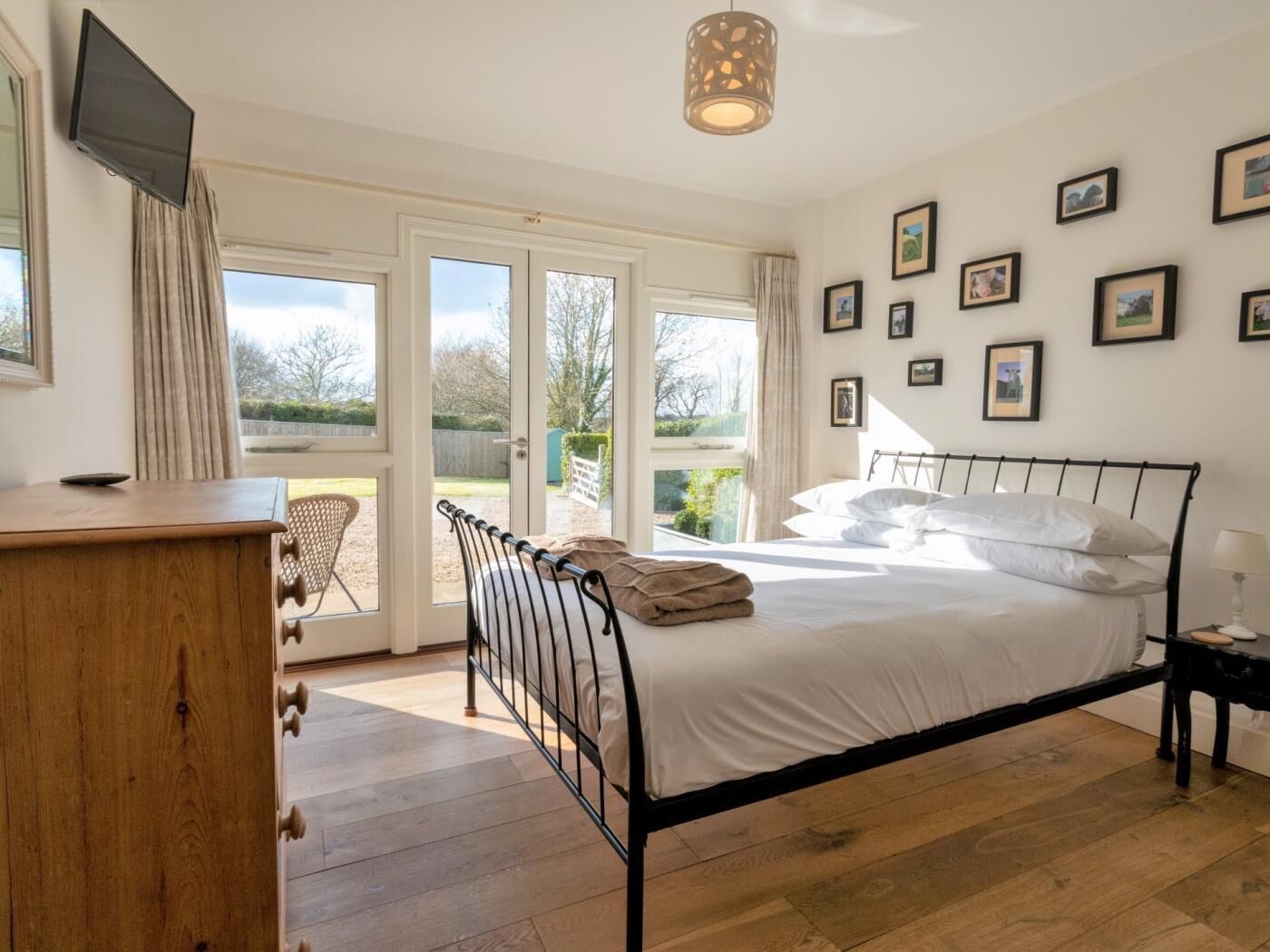 A bedroom with a bed, a wooden dresser, a television, and a large window.