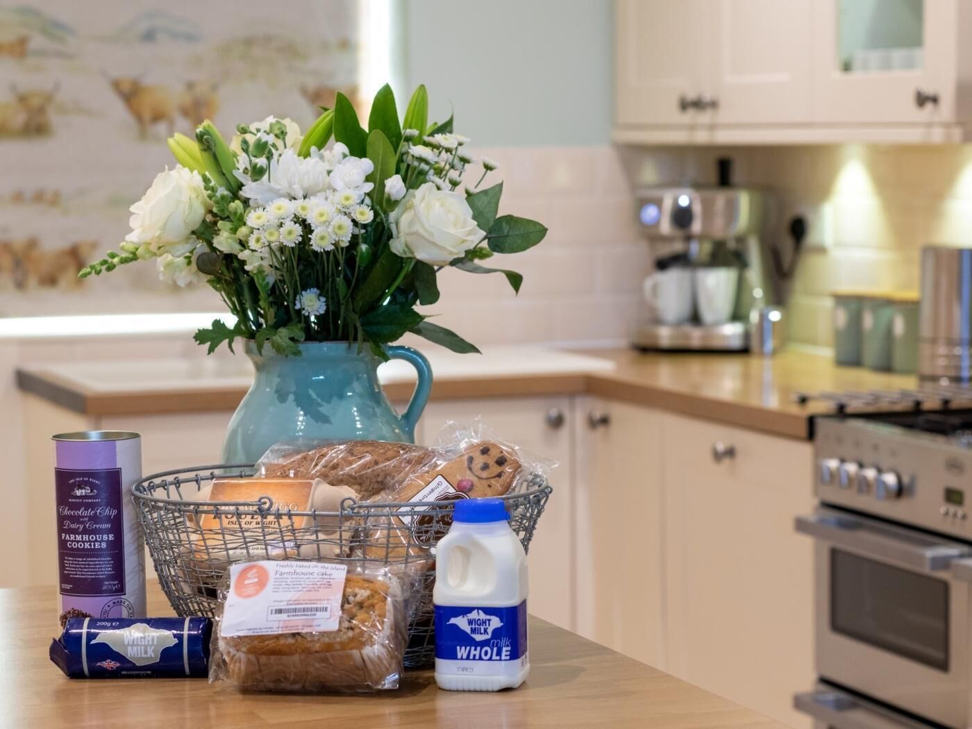 Un comptoir de cuisine orné d’un vase de fleurs, d’un panier rempli de produits de boulangerie, d’un carton de lait et d’une boîte de biscuits.
