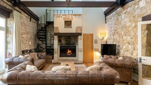 A cozy living room with a fireplace, leather sofas, a staircase, and stone walls. - 4 Bed in Bembridge (oc-ic130) (Hillway)