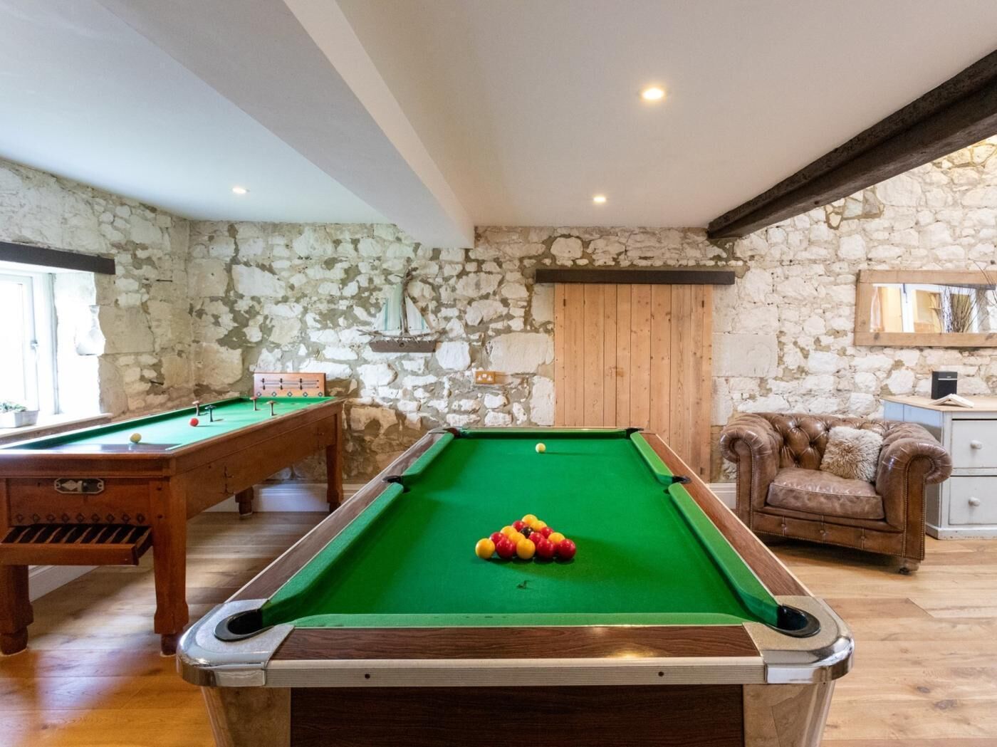Una mesa de billar con bolas, un sofá y una pared de piedra.