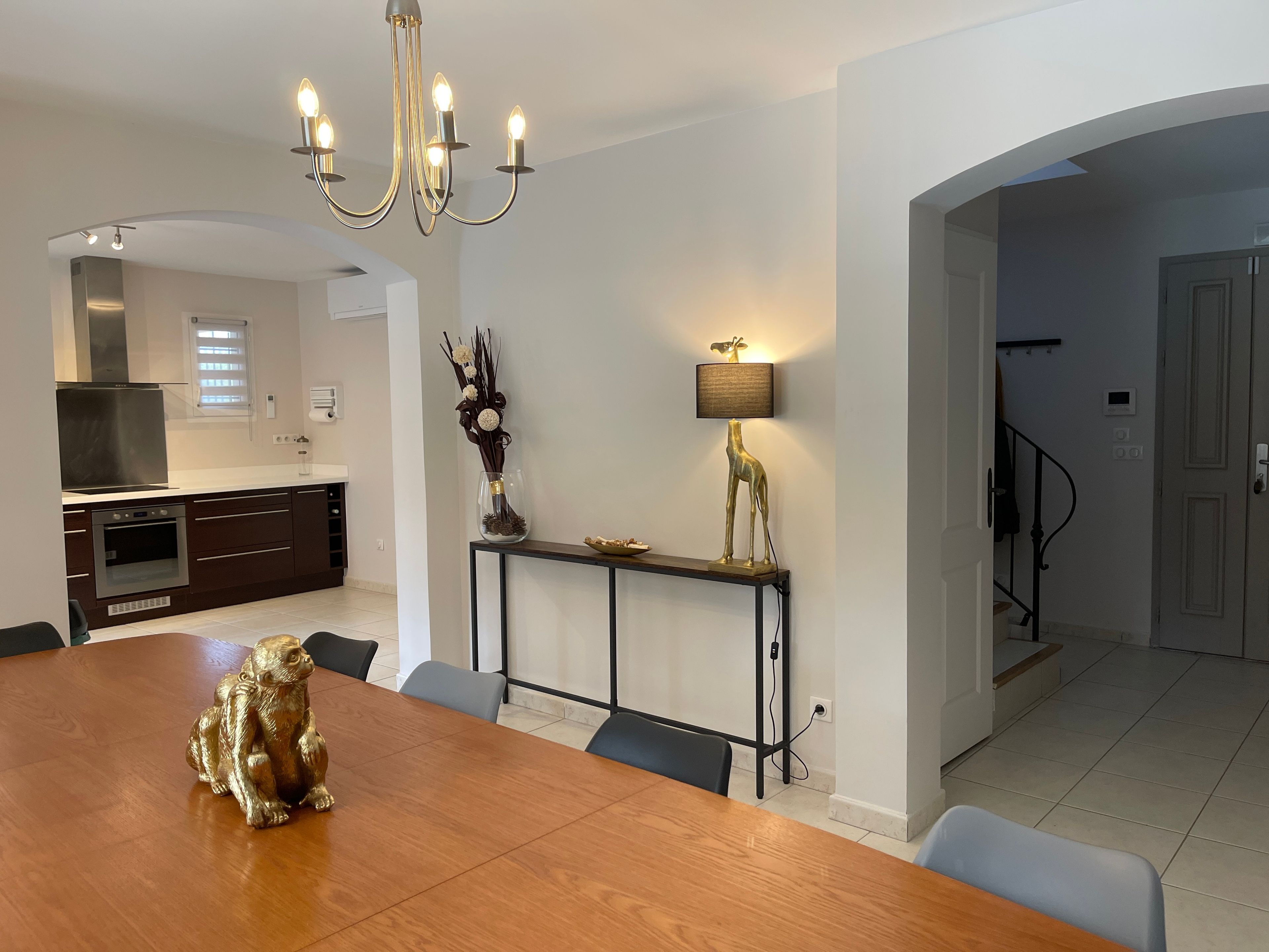 A modern kitchen with a dining area, a chandelier, a decorative lamp, and a statue on the table.