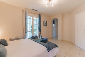 Et hotelværelse med en seng, en radiator, gardiner, et indrammet billede og en gang, der fører til et andet værelse.