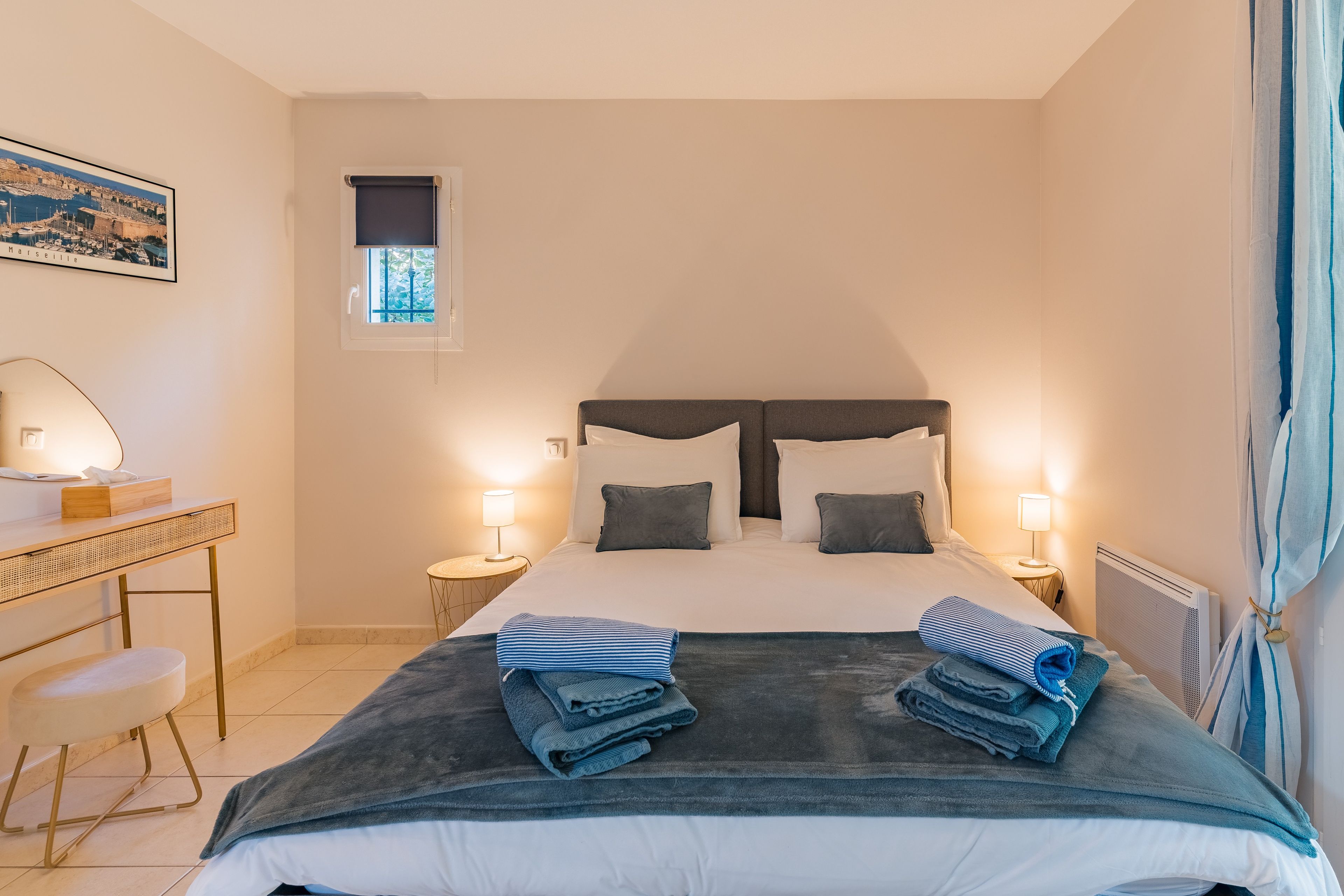Ein Hotelzimmer mit Bett, Nachttischen, Schreibtisch, Stuhl, Fenster und Heizkörper.