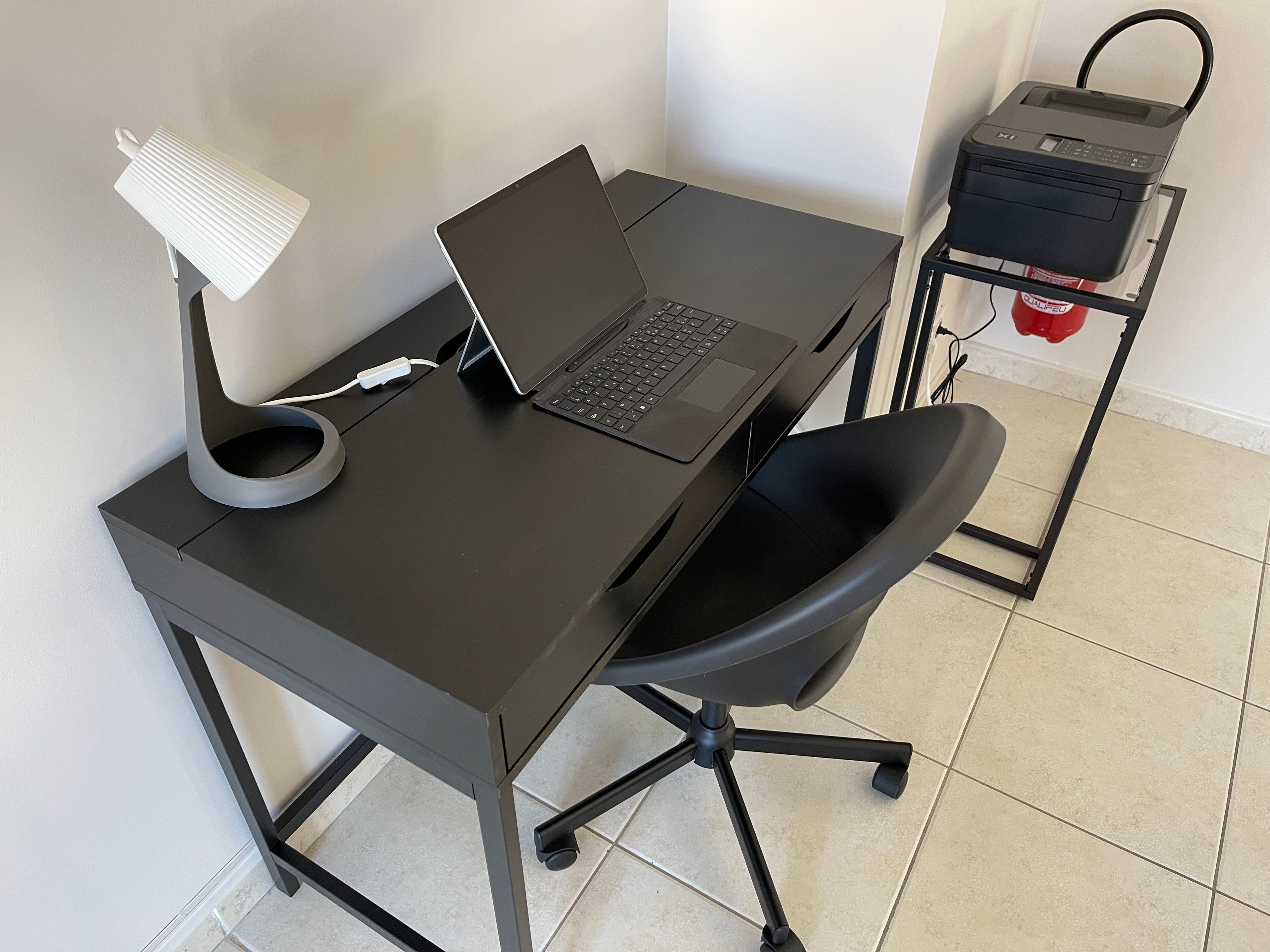 A black desk with a laptop, a white desk lamp, and a black office chair.