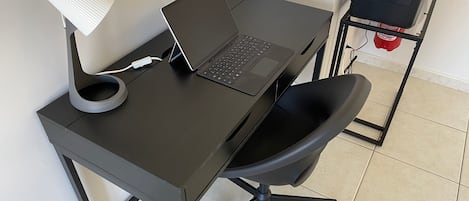 Un escritorio negro con una computadora portátil, una lámpara de escritorio blanca y una silla de oficina negra.