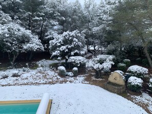 Ein mit Schnee bedeckter Garten mit Bäumen und einem Steinbau.