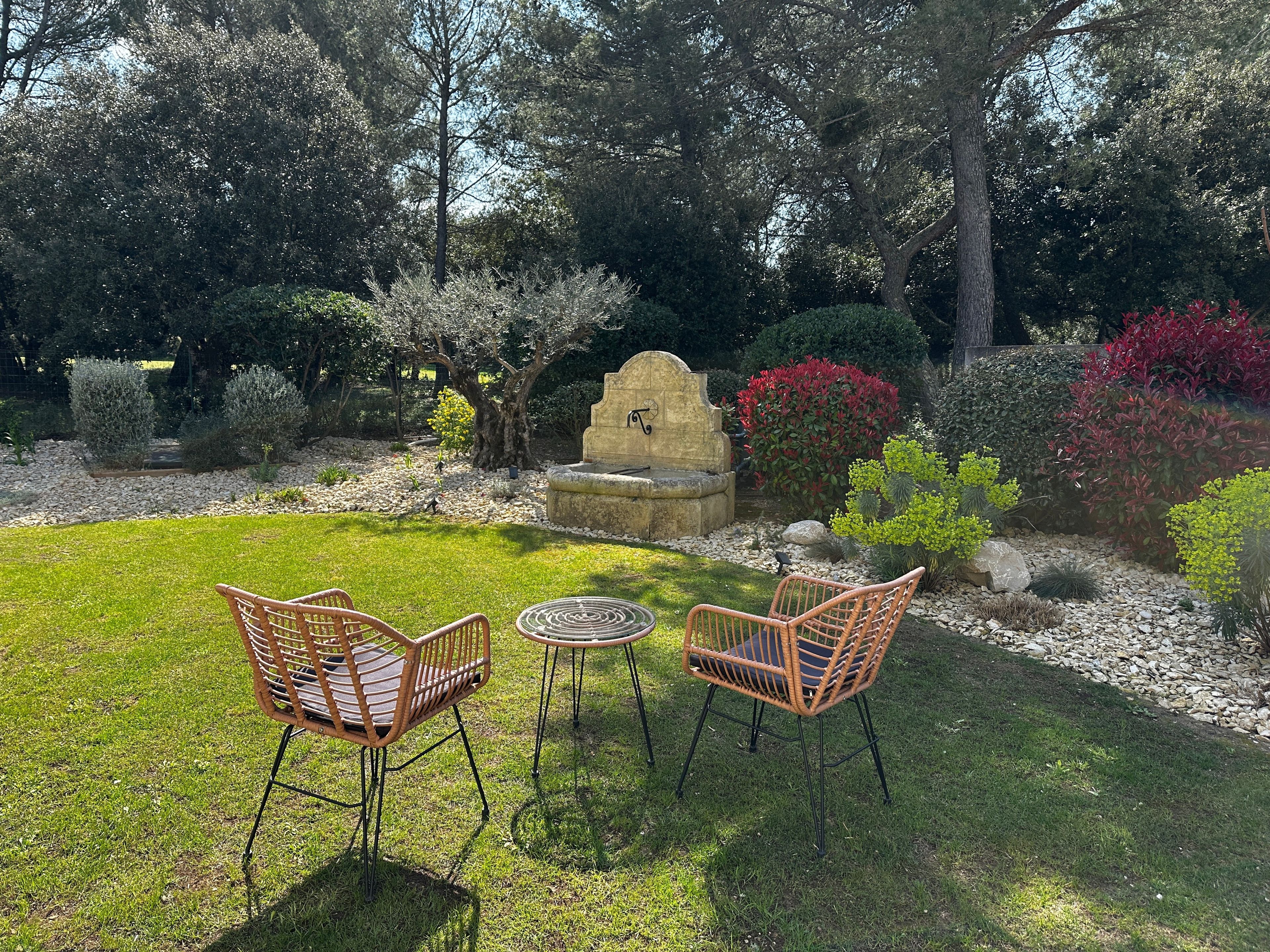 A garden with a stone fountain, two wicker chairs, and a small round table.