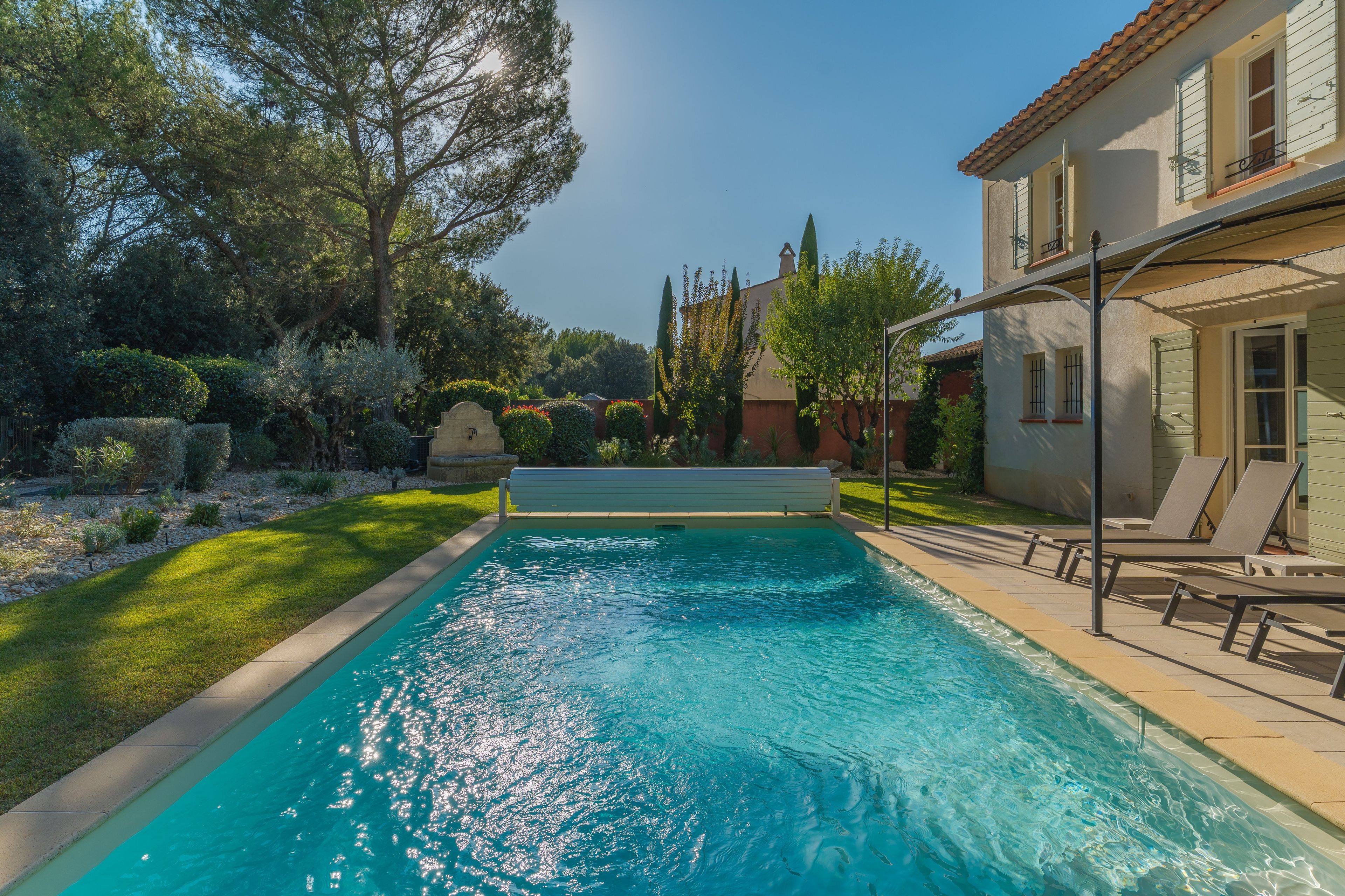 Une piscine à l’eau d’un bleu cristallin, entourée d’une pelouse bien entretenue et de divers arbres.