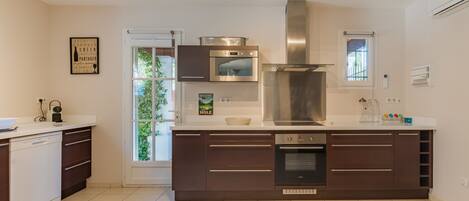 A modern kitchen with a central island, stainless steel appliances, and a view of greenery outside.