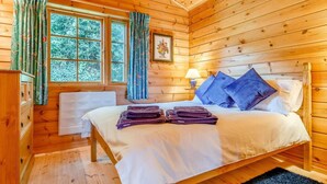Ein Schlafzimmer in einer Holzhütte mit einem Bett, Vorhängen, einem Fenster und einer Lampe.