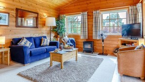 Ein Innenraum einer Blockhütte mit einem blauen Sofa, einem Holztisch, einem Fernseher und einem Kaminofen.