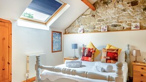 A bedroom with a stone wall, a skylight, a bed with white bedding, and a wooden wardrobe. - 2 Bed in Godshill (oc-ic129) (Godshill)