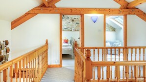 A high-ceilinged room with wooden beams, a staircase, and a view into another room with a bed and a stone wall. - 2 Bed in Godshill (oc-ic129) (Godshill)