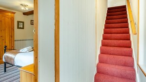 Hotellihuone, jossa on sänky, puinen vaatekaappi, punaisella matolla päällystetty portaikko ja valkoinen seinä.