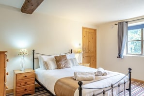 Ein Schlafzimmer mit einem Bett, Nachttischen, einem Kleiderschrank, einem Fenster mit Vorhängen und einem Holzbalken an der Decke.