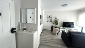 Ett modernt vardagsrum med en TV, en soffa och en matplats med en vit bänkskiva och en spegel.