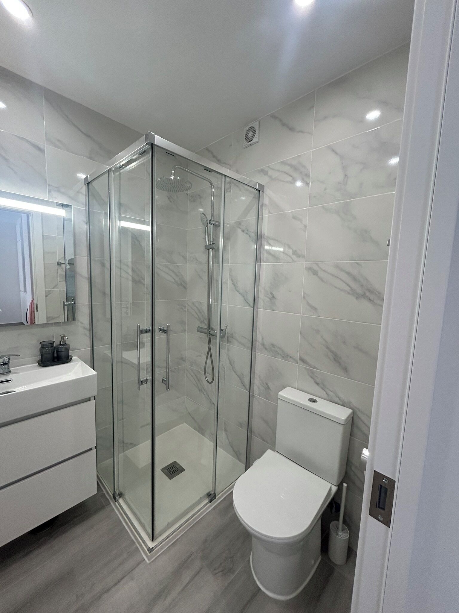Une salle de bain moderne avec une douche à parois de verre, des toilettes blanches et un meuble-lavabo avec un miroir.