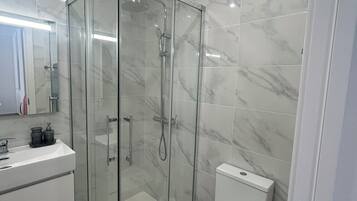 Une salle de bain moderne avec une douche à parois de verre, des toilettes blanches et un meuble-lavabo avec un miroir.