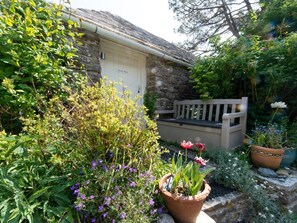 A stone building with a white door labeled 'Stone Barn,' surrounded by lush greenery and potted plants. - 1 Bed in Swanage (oc-ic131) (Worth Matravers)
