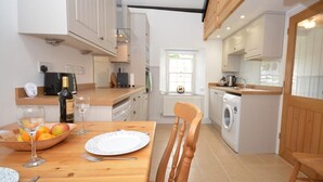 A compact kitchen with a dining area, a washing machine, and a window with a view. - 1 Bed in Haverfordwest (oc-61170) (Porthgain)