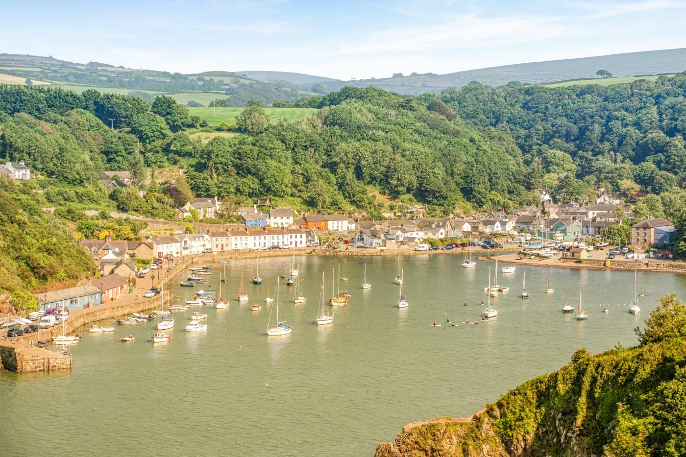A coastal town with a marina filled with boats, surrounded by lush greenery and hills.