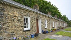 A stone building with a row of windows and doors, potted plants, and a stone pathway. - 1 Bed in Haverfordwest (oc-61170) (Porthgain)