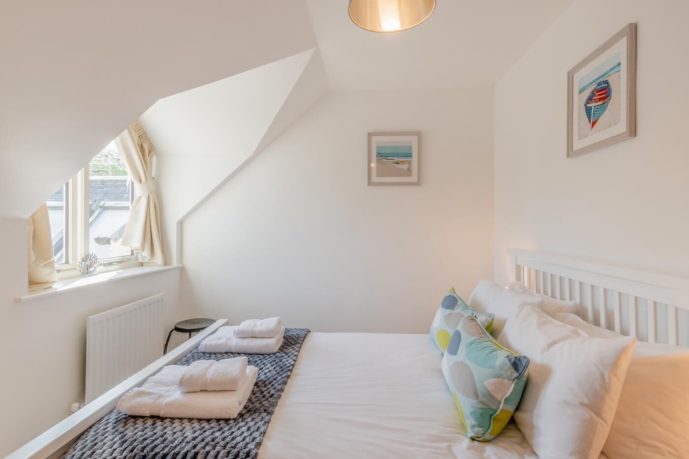 A bedroom with a bed, a window, a radiator, and a framed picture on the wall.