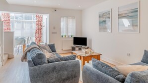 Ein modernes Wohnzimmer mit einer Sofagarnitur, einem Fernseher und einem Essbereich mit Tisch und Stühlen.