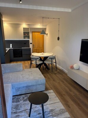 Ein modernes Wohnzimmer mit Sofa, Esstisch mit Stühlen, Küchenzeile und Wandfernseher.