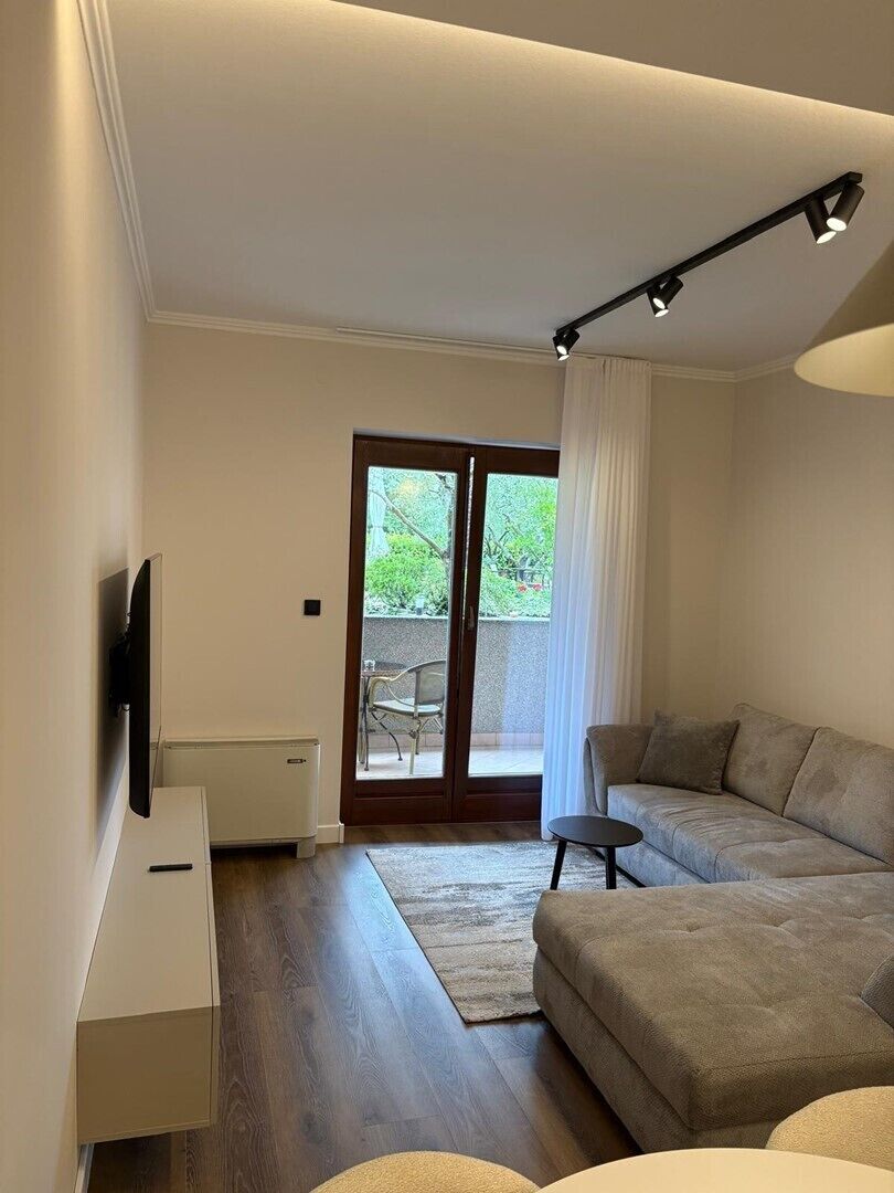 A modern living room with a sofa, a small table, a flat-screen TV, and a sliding glass door leading to an outdoor area.