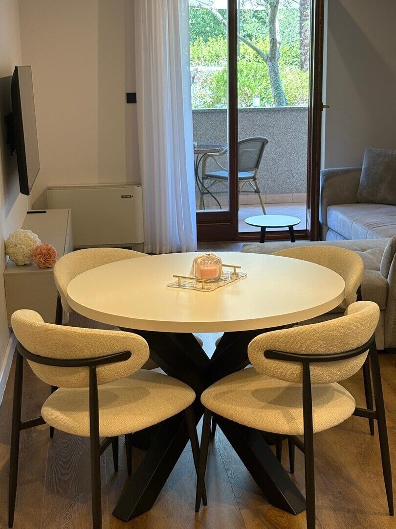 A round dining table with four chairs, a small table with a candle, a sofa, a TV, and a sliding glass door leading to an outdoor area.