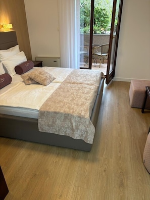 Ein Schlafzimmer mit einem Bett, einem Nachttisch, einem Sessel und Blick ins Freie.