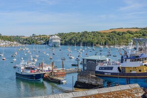 A harbor with multiple boats docked, a prominent white building, and a hilly landscape in the background. - 2 Bed in Polruan (oc-pc023) (Fowey)