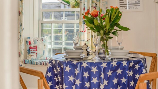 Une table à manger recouverte d’une nappe bleue, mise avec des assiettes, des verres et un vase de fleurs.