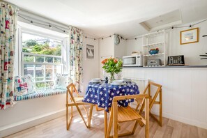 A dining area with a table set for two, a window seat, and a kitchen area with appliances. - 2 Bed in Polruan (oc-pc023) (Fowey)