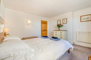 A bedroom with a large bed, a wooden door, a dresser, and a radiator. - 2 Bed in Polruan (oc-pc023) (Fowey)