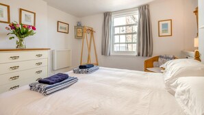 Une chambre à coucher avec un lit, une commode, une fenêtre avec des rideaux, un radiateur et des tableaux encadrés accrochés au mur.